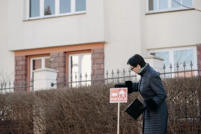 Real estate agent in a black coat placing a 'For Sale' sign in front of a house. Real Estate Social Media Mistakes and Lead Conversion